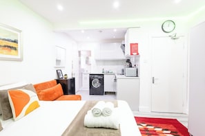Habitación de hotel con cama, sofá, lavadora, microondas y un reloj en la pared.