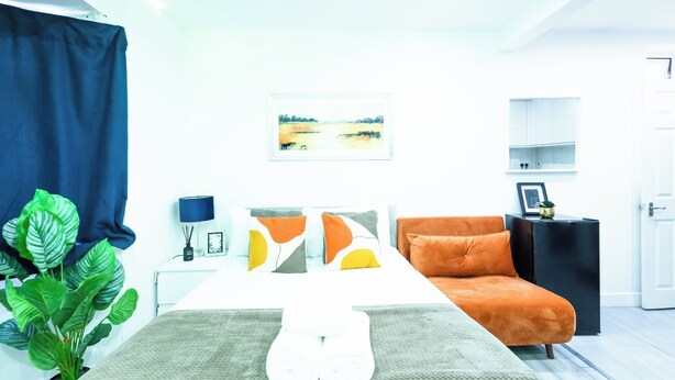 Ein modernes Schlafzimmer mit Bett, Nachttisch, Lampe, Sofa und einem Gemälde an der Wand.