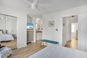 A bedroom with a bed, a bench, a ceiling fan, a TV, a kitchen area, and a bathroom. - Prime Location/2 Bdr/Sleeps 7/Pet friendly (Santa Rosa Beach)