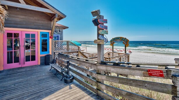 A wooden deck with a pink door, a wooden fence, and a signpost with multiple directional signs. - Prime Location/2 Bdr/Sleeps 7/Pet friendly (Santa Rosa Beach)