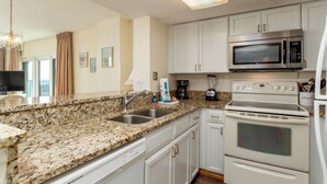 A kitchen with granite countertops, white cabinets, a microwave, stove, and a coffee maker. - Two oceanfront units, side by side. Perfect for extended family and golf group vacations (Myrtle Beach)