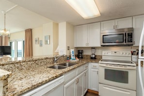 A kitchen with granite countertops, white cabinets, a microwave, stove, and a coffee maker. - Two oceanfront units, side by side. Perfect for extended family and golf group vacations (Myrtle Beach)