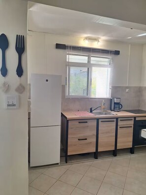 Eine Küche mit Kühlschrank, Spüle, Kaffeemaschine und einem Fenster mit Jalousien.