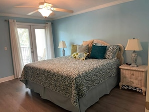 A bedroom with a bed, two bedside tables, a ceiling fan, and a window with curtains.