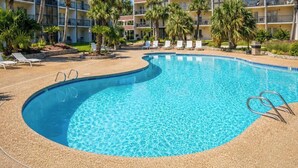 Una piscina con sillas de descanso y palmeras, rodeada por un edificio con balcones.