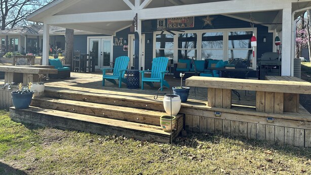 Een overdekt buitengebied met blauwe Adirondack-stoelen, een houten bank en een barbecue.