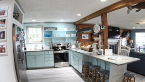 Een keuken met een centraal eiland, barkrukken en een koelkast.