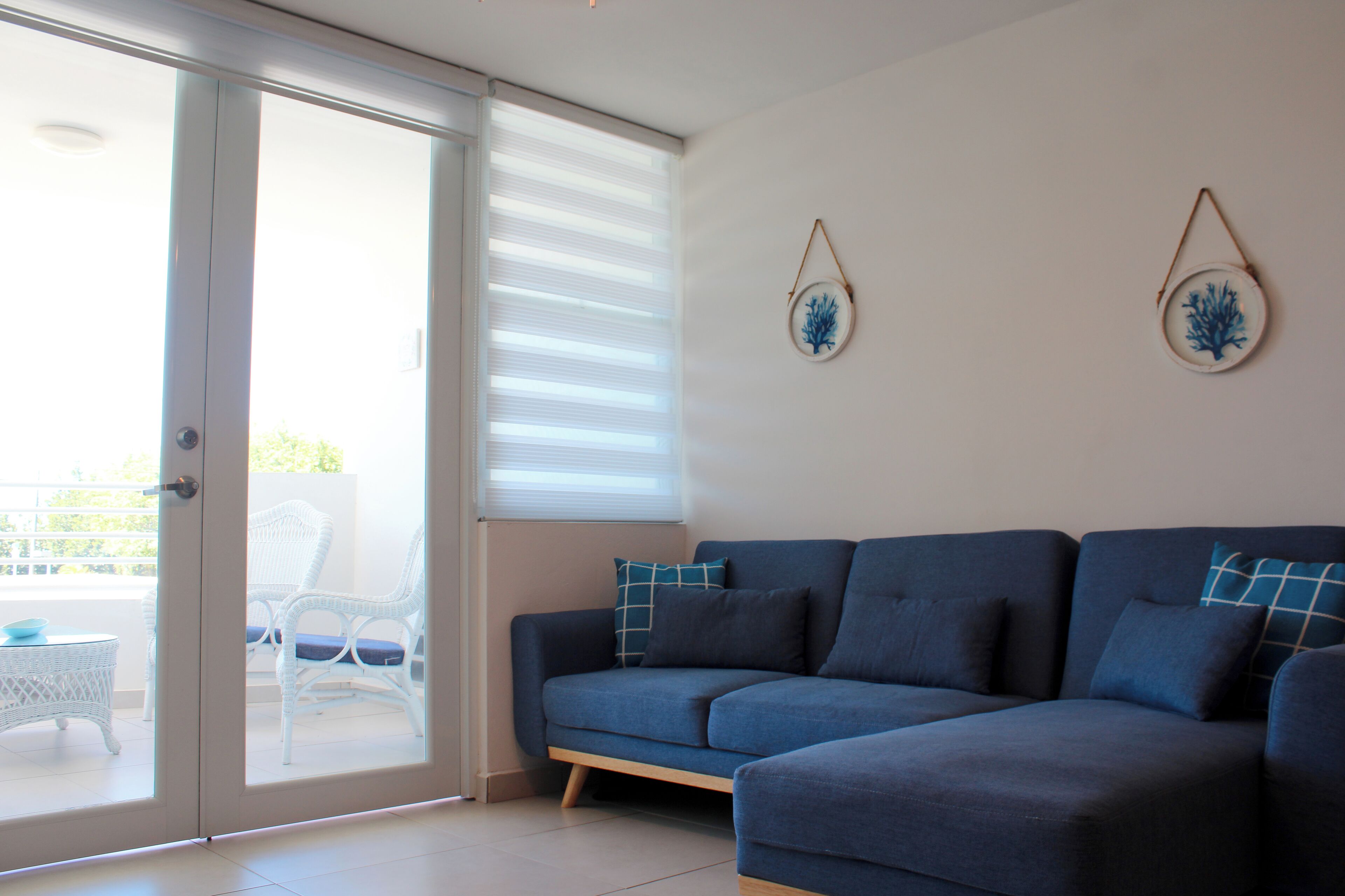 Un saló amb un sofà blau, cadires de vimetra blanca i una porta de vidre que dona a una zona exterior.