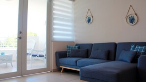 Un salon avec un canapé bleu, des fauteuils en osier blancs et une porte en verre donnant sur un espace extérieur.