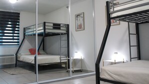 Une chambre avec deux lits superposés, une porte-fenêtre coulissante, une petite table de chevet avec une lampe et un tableau encadré au mur.