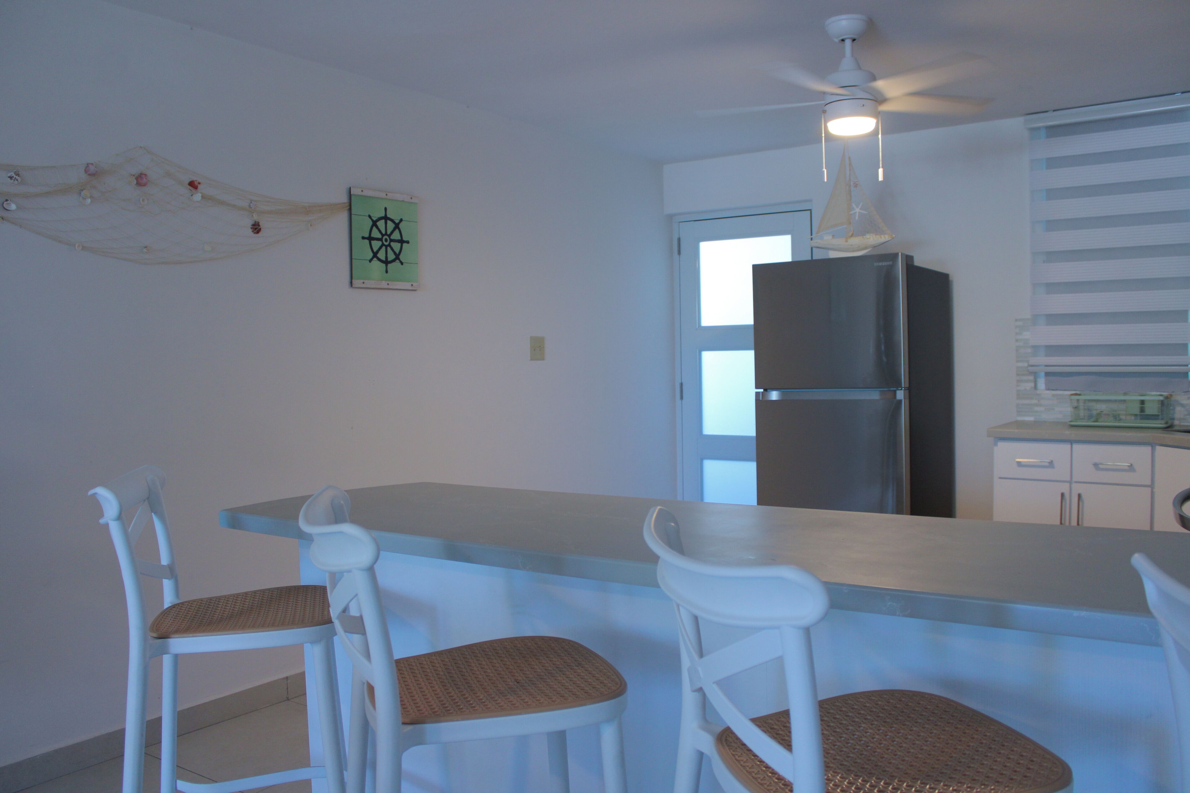 A kitchen with a central island, white chairs, a refrigerator, and a ceiling fan.
