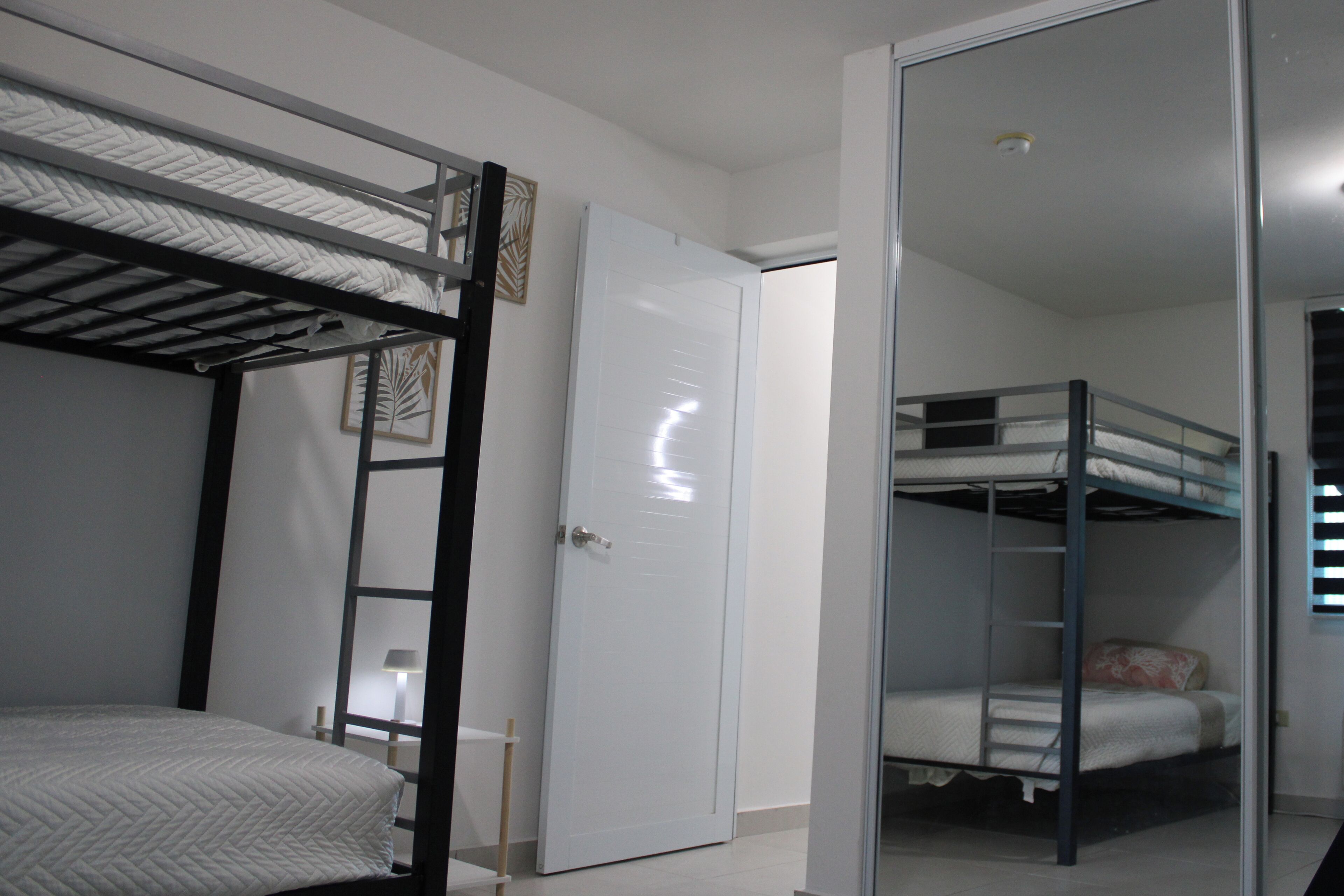 A bedroom with bunk beds, a white door, and a mirror.