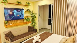 A hotel room with a bed, a sofa, a TV, and a plant. - Apartaloft Green Paradise - Santa Marina (Santa Marta)