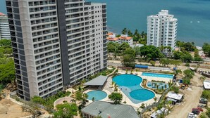 A high-rise hotel with multiple balconies overlooking a coastal area, featuring a pool complex with three distinct swimming areas. - Apartaloft Green Paradise - Santa Marina (Santa Marta)