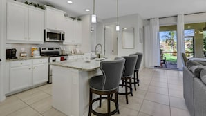 Una cocina moderna con armarios blancos, una isla central con taburetes de bar, un microondas y una estufa.