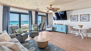 Ein geräumiges Wohnzimmer mit Blick auf den Strand, einem Deckenventilator, einem Flachbildfernseher und einem Essbereich mit Korbstühlen.