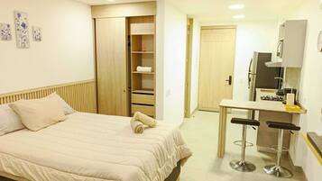 A bedroom with a bed, a closet, a kitchenette, and a bathroom.