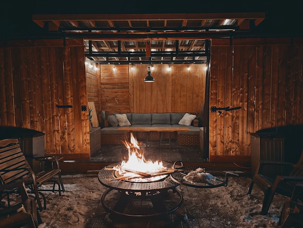 A cozy outdoor seating area with a fire pit, wooden walls, and a cushioned bench. - Mirrored Waters Ranch Cabin (Mirror)