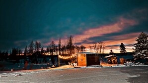 En stuga av trä med en möblerad uteplats under tak och ett litet förråd.