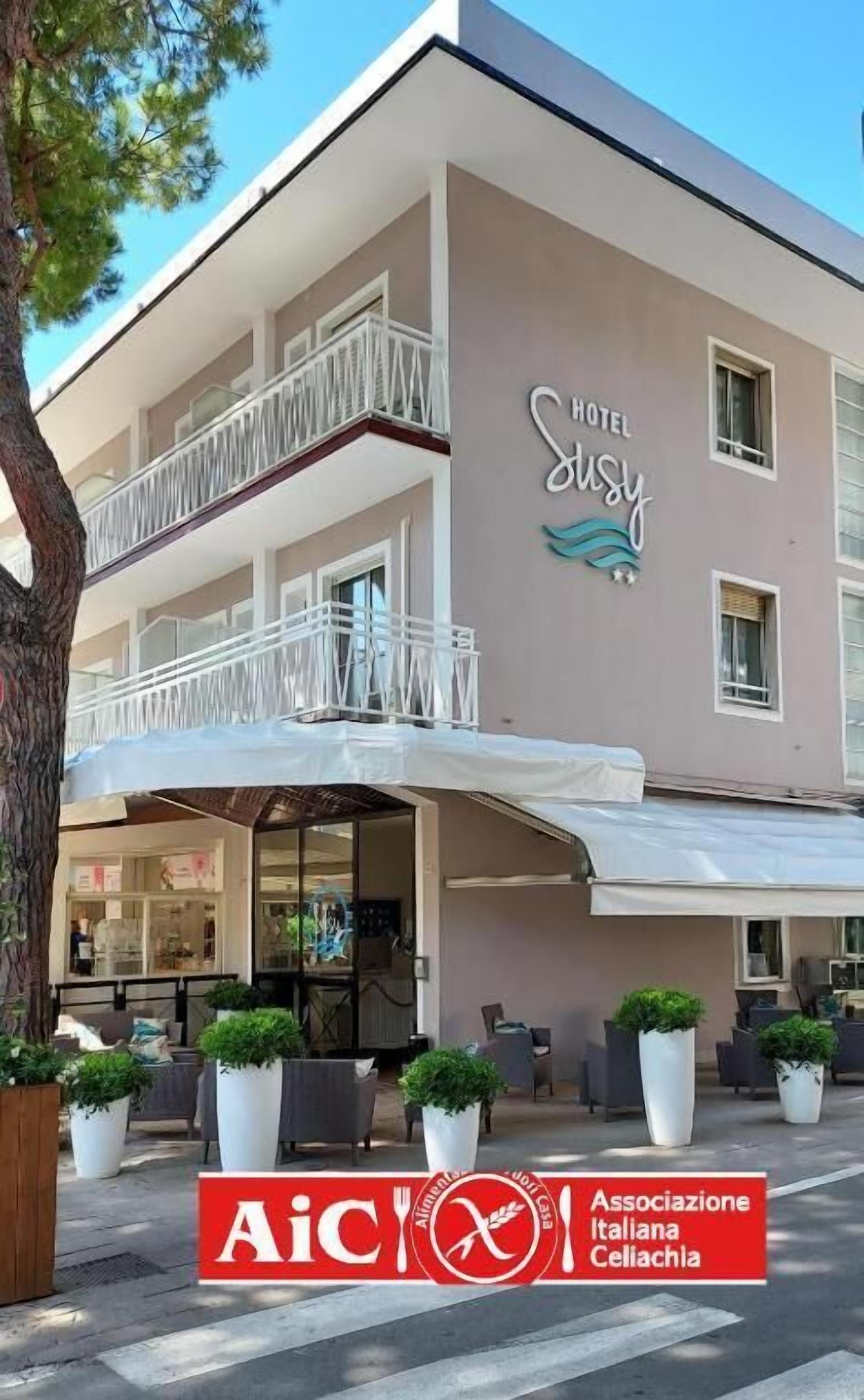 Edifici de dues plantes amb un rètol que diu 'HOTEL Sussy' i una zona d'estar a l'aire lliure coberta, decorada amb plantes en testos.