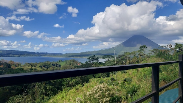 Vista de un lago, una montaña y follaje circundante desde un balcón.