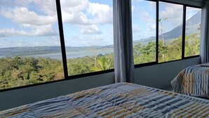 Un dormitorio con un amplio ventanal que ofrece vistas a un paisaje montañoso y una masa de agua.