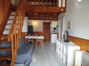 A compact living space with a wooden staircase, a dining area, and a kitchenette. - One-bedroom apartment with mezzanine and terrace - sleeps 6 - 6PORTO23 (SAINT CYPRIEN PLAGE)