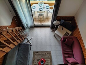 Ein kompakter Wohnraum mit einer Holztreppe, einer Couch, einem Couchtisch und einem Essbereich mit Tisch und Stühlen.