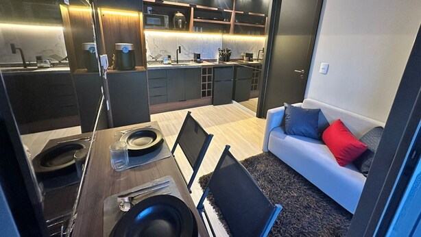 A compact living space with a dining area, kitchenette, and a sofa with cushions. - Luxurious 1-bedroom apartment in Pinheiros. AC, gym, pool, prime location (São Paulo)