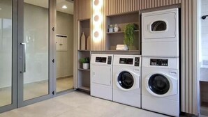 A modern laundry room with built-in appliances, a glass door entrance, and a wooden ceiling. - Luxurious 1-bedroom apartment in Pinheiros. AC, gym, pool, prime location (São Paulo)