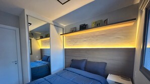 A modern bedroom with a large bed, a bedside table, a nightstand, a mirror, and a shelf with books. - Luxurious 1-bedroom apartment in Pinheiros. AC, gym, pool, prime location (São Paulo)