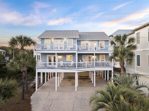 A two-story house with a balcony, palm trees, and a clear sky. - New Kulula EAST - 3 BR Short walk to the beach, heated pool, Sleeps 9 (Santa Rosa Beach)