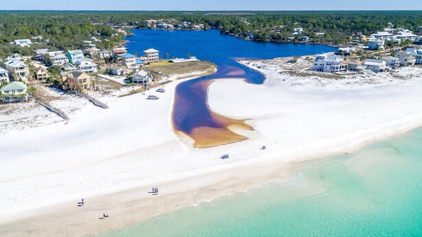 Vista aérea de una zona costera con playa, aguas turquesas cristalinas y un río que desemboca en el mar.