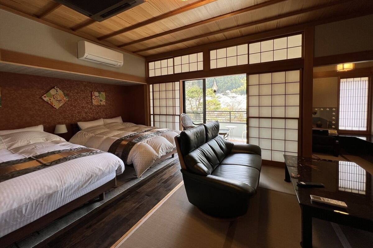 A traditional Japanese-style room with tatami flooring, a tatami mat table, a black leather sofa, and a sliding shoji screen door.