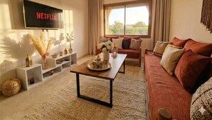A living room with a TV displaying 'NETFLIX', a sofa, a coffee table, and a window with curtains. - Bohemian chic in the heart of the red city with swimming pool (Marrakech-Safi)
