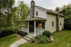 A two-story house with a stone chimney, a covered porch, and a stone pathway leading to the entrance.