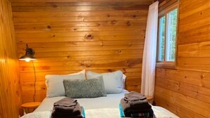 Una habitación de cabaña de madera con una cama, una mesita de noche, una lámpara y una ventana.