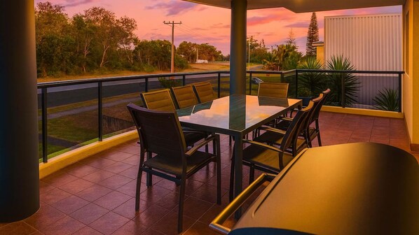 Un balcon avec une table et des chaises, une vue sur une route et un coucher de soleil.