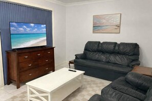 Una sala de estar con televisor, sofá, mesa de centro y un cuadro en la pared.
