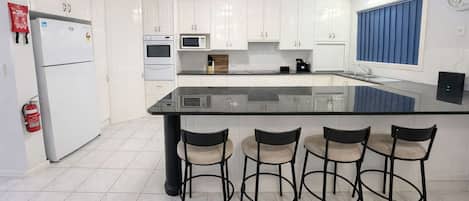 A modern kitchen with white cabinets, a black countertop, and four bar stools.