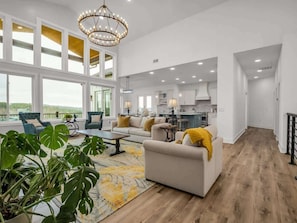 Ein geräumiges Wohnzimmer mit großen Fenstern, einer Kristallleuchtre und Blick ins Freie.