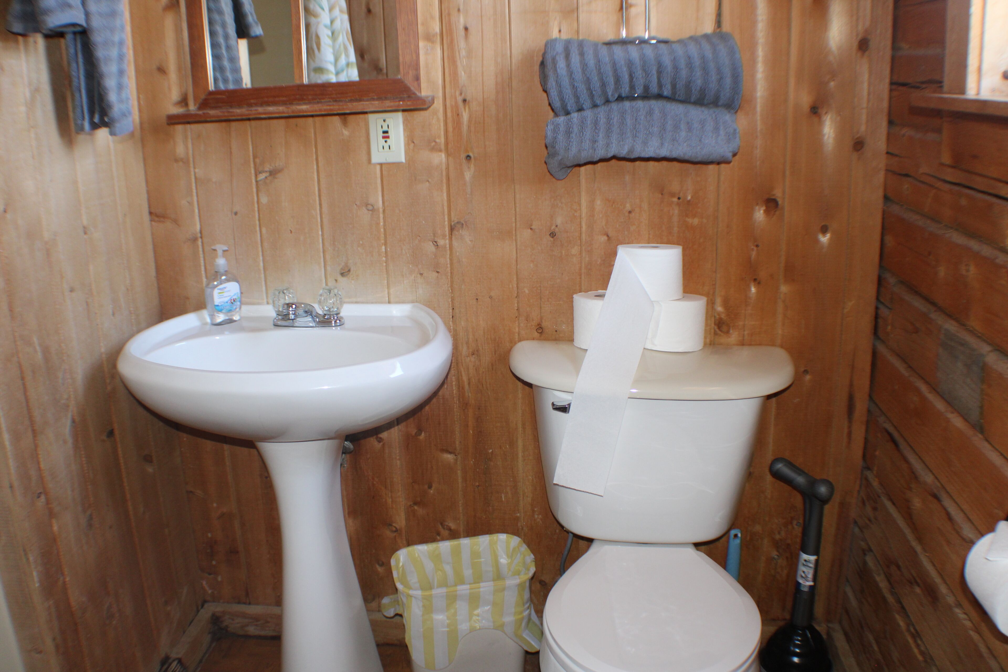 Et badeværelse i træ med vask, toilet og moppe.