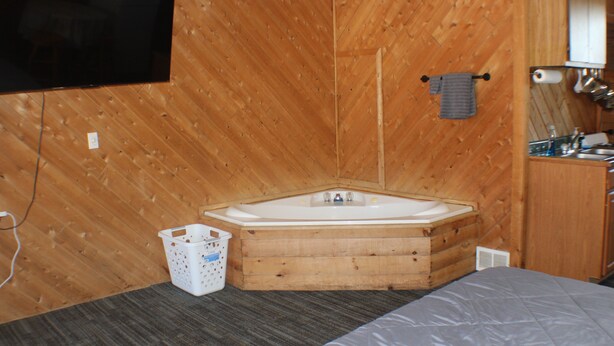 Una stanza piccola e accogliente con pavimento in legno, un letto singolo, una vasca in legno, un lavandino e una TV a schermo piatto fissata alla parete.