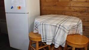Una stanza piccola con un frigorifero bianco, un tavolo di legno con tovaglia a quadri e due sgabelli di legno.
