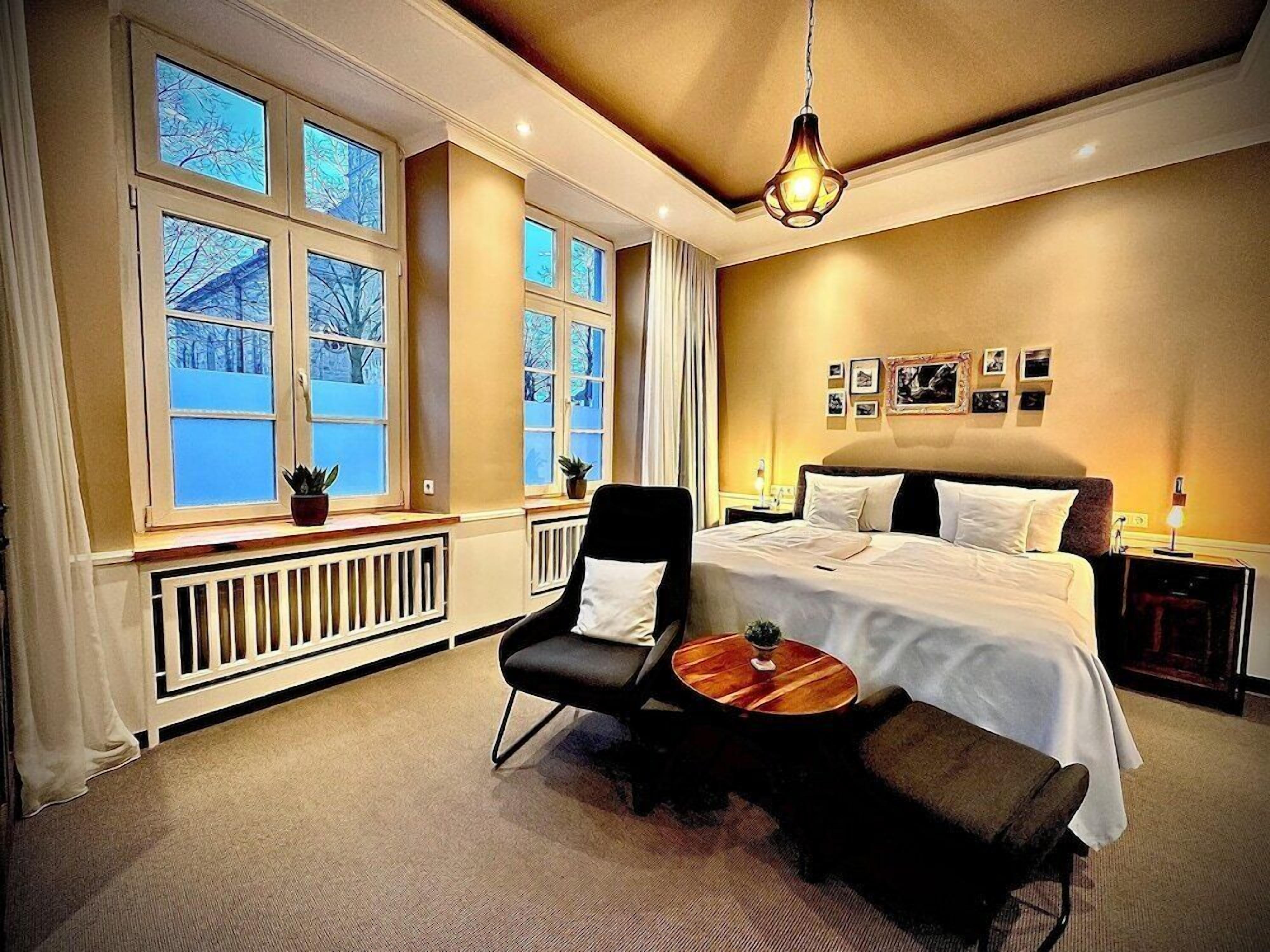 Ein Hotelzimmer mit einem großen Bett, einem Sessel, einem kleinen Tisch und einem Fenster mit Blick auf Bäume.