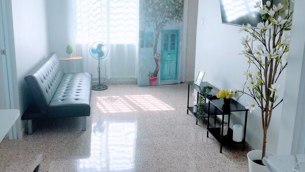 A modern living room with a sofa, a standing fan, a TV, and a potted plant. - 2-bedroom, walk to the beach, reserved parking, AC in each bedroom (San Juan)