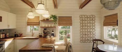 A kitchen with wooden beams, pendant lights, a central island, a coffee machine, and a view of the outdoors.