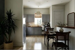A modern kitchen with grey cabinets, a wooden dining table, and a hanging light fixture. - 30A Carriage House | 5 min to beach | Cart & Bikes (Santa Rosa Beach)