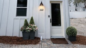 Un edificio blanco con el número "222" en la puerta, un pequeño porche con plantas en macetas y un camino de entrada de grava.