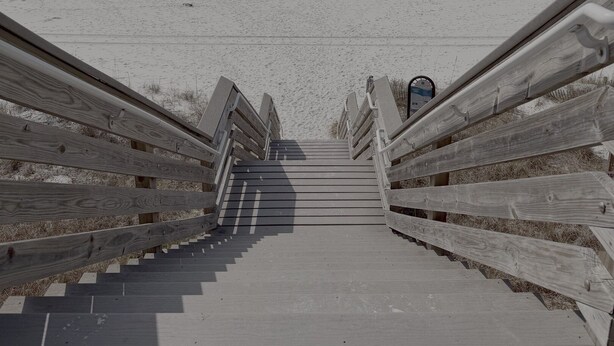 Una escalera de madera que lleva a una playa, con vista despejada al océano.